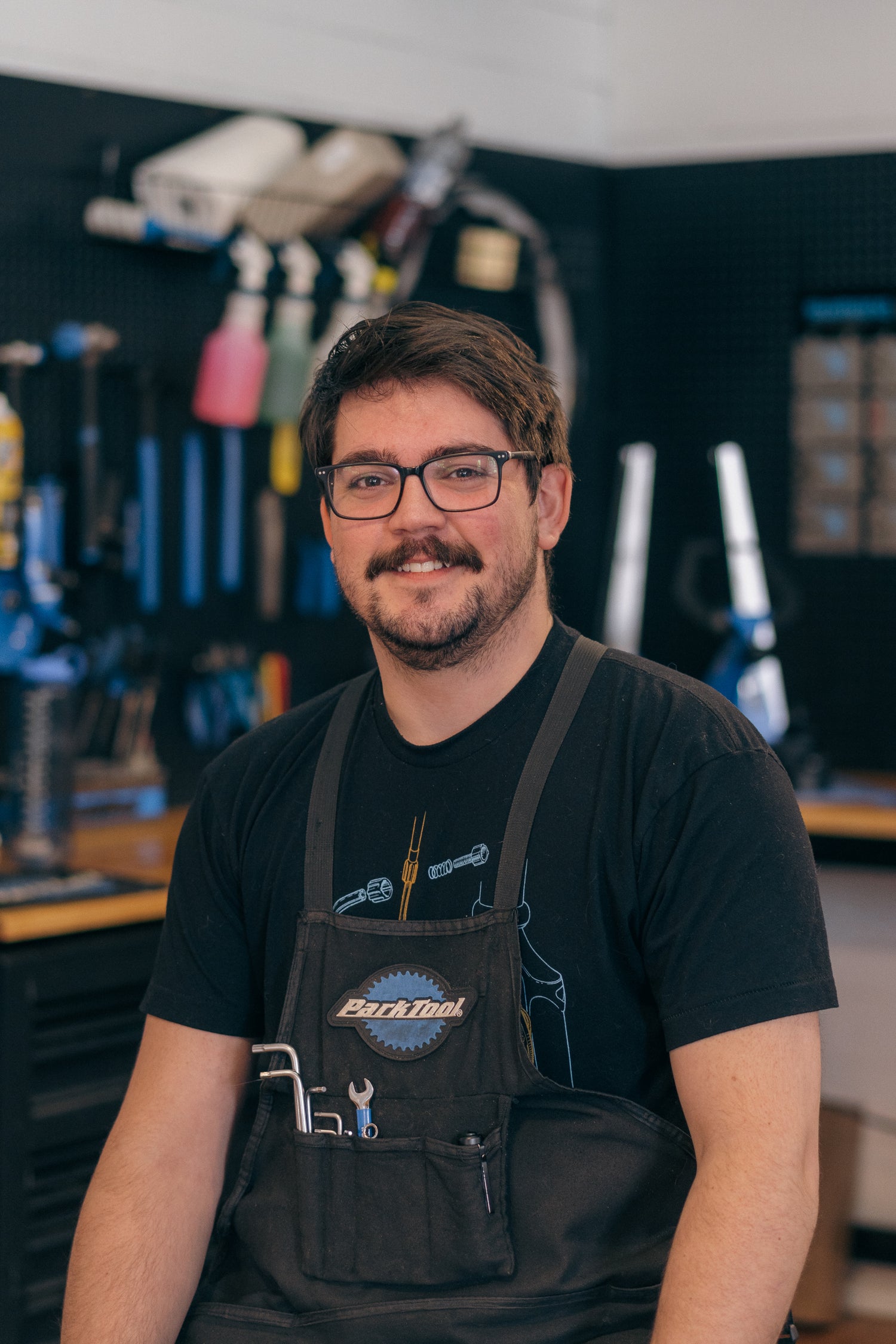 Man wearing a black apron with a tool belt in a workshop setting